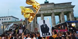 Viele Menschen mit Plakaten und goldenen Fahnen, zwei Wagen vor dem Brandenburger Tor