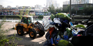 ein Bulldozer schiebt viele Zelte und Matratzen zusammen