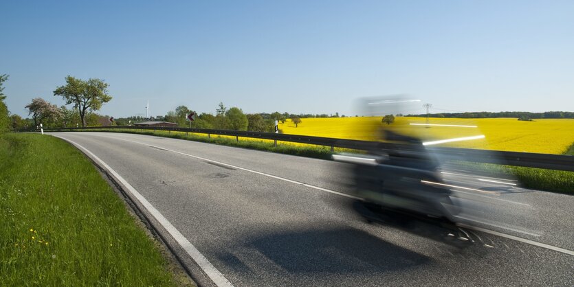 ein Motorrad braust über eine Landstraße - es ist verwischt zu sehen, da mit längerer Belichtungszeit aufgenommen