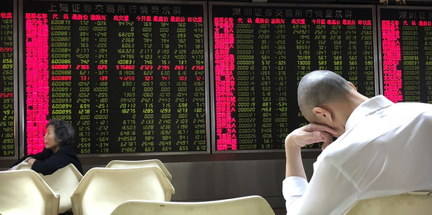 Ein Mann hat den Kopf aufgestützt und sitzt vor einer Börsentafel