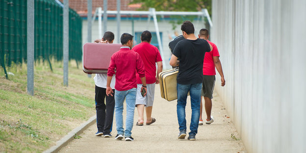 Flüchtlinge laufen mit Koffern bepackt auf einem Weg einer Erstaufnahmeeinrichtung für Flüchtlinge