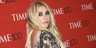 Sängerin Kesha steht vor einer roten Wand