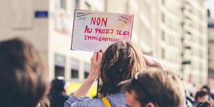 Eine Frau hält ein französisches Plakat auf einer Demo gegen leichtere Abschiebung hoch