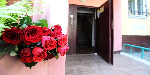 Ein Bund Rosen an einem Pfeiler am Eingang eines Hauses. Die Haustür steht offen