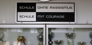 Das Logo von "Schule ohne Rassismus" hängt über einem Schrank voller Pokale