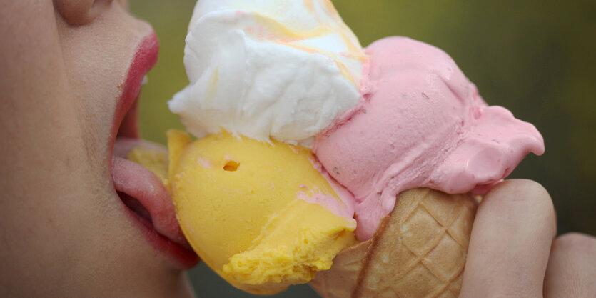 Drei Kugeln Eis in der Waffel und ein Kindermund mit leckender Zunge