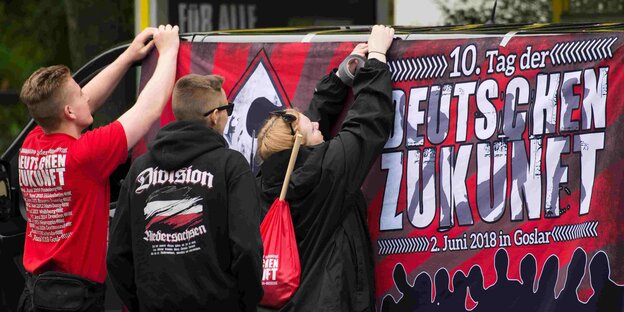 Drei junge Menschen befestigen ein Banner an einem Transporter