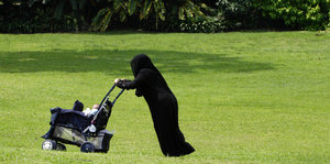 Eine Person in einer Burka schiebt einen Kinderwagen