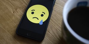Ein Facebook-Smiley mit Tränen auf einem Smarphone neben einer Kaffeetasse
