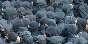 Viele vermummte Menschen in schwarzer Kleidung und Sonnebrillen