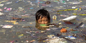 Junge schwimmt in Wasser voller Abfälle