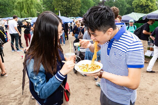 Zwei Menschen essen im Stehen mit Stäbchen von einem Plastik-Teller Zwei Menschen essen im Stehen mit Stäbchen von einem Plastik-Teller