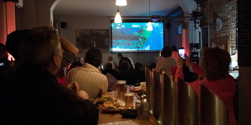 Menschen von hinten, die auf eine Leinwand mit Eishockey schauen, Pommes auf dem Tisch