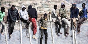 Afrikanische Migranten sitzen auf dem Grenzzaun zwischen Marokko und der spanischen Exklave Ceuta