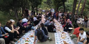 Muslime und Atheisten sitzen sich beim Iftar Papierbahnen gegenüber, die auf dem Boden ausgebreitet sind und auf denen Essen steht