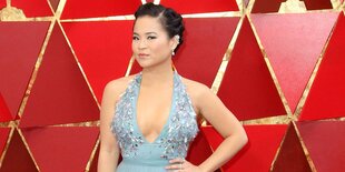 Die Schauspielerin Kelly Marie Tran steht in einem Kleid vor einer roten Wand und posiert für Fotografen