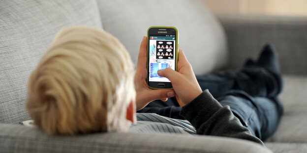 Ein Kind liegt auf einem Sofa und blickt auf ein Handy