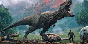 Links ein Dinosaurier, rechts kauern sich ein Mann, eine Frau und ein Mädchen ängstlich am Boden