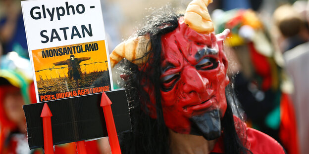 Ein als Teufel kostümierter Aktivist protestiert mit dem Schild "GlyphoSATAN" vor der Bayer-Konzernzentrale gegen die Fusion mit Monsanto