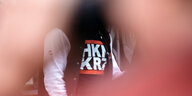 Durch ein von Hände gebildetes Loch ist en T-Shirt mit der Aufschrift „HKNKRZ“ zu sehen