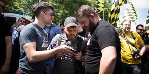 Martin Sellner und zwei andere Männer gucken bei einer Demonstration auf ein Smartphone