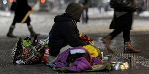 Ein Obdachloser sitzt auf einem Schlafsack auf der Straße
