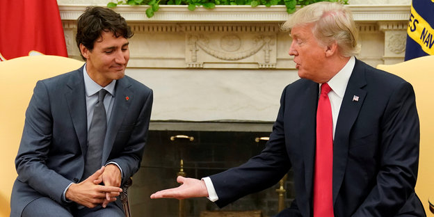 Zwei Männer sitzen nebeneinander, der eine ist Donald Trump und reicht dem anderen die Hand. Dieser macht keine Anstalten, die Hand zu nehmen. Es ist Kanadas Premierminister Justin Trudeau