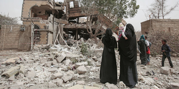 Zwei Frauen, eine mit einem Kind auf dem Arm, stehen in einer zerbombten Stadt