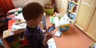Ein Kind steht in einem Kinderzimmer mit Spielsachen und spielt auf seinem Smartphone