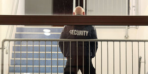 Ein kräftiger Mann mit Glatze und Security-Schriftzug auf der Jacke steht vor einem Treppenaufgang