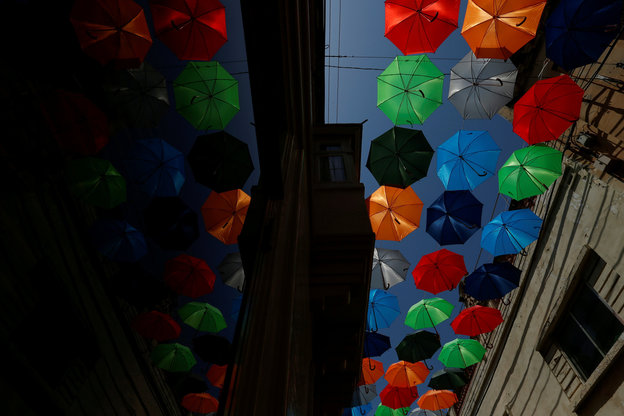 Eine Girlande aus bunten Regenschirmen hängt über einer Straßengasse