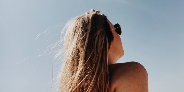 Eine Frau trägt Sonnenbrille und guckt in den blauen Himmel