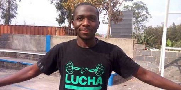 Ein Mann im schwarzen T-Shirt mit grüner Aufschrift breitet lächelnd beide Arme aus
