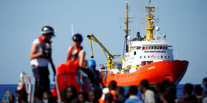 Das Rettungsschiff "Aquarius" mit geretteten Menschen auf einem Boot im Vordergrund