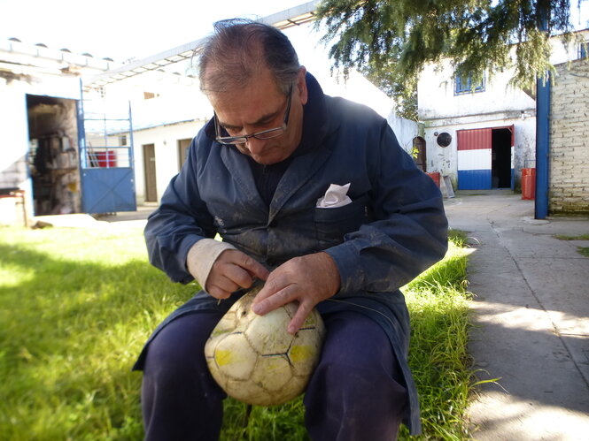 Ein Mann sitzt in einem Innenhof und näht an einem Ball