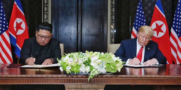 Donald Trump und Kim Jong Un schreiben an einem Tisch