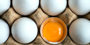 Ein aufgeschlagenes Ei liegt zwischen anderen weißen Eiern in einem Karton