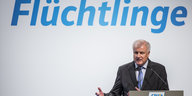 Innenminister Horst Seehofer stitzt unter dem Schriftzug "Flüchtlinge"