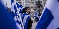 Eine Frau hält auf einer Demonstration sehr viele griechische Flaggen