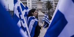Eine Frau hält auf einer Demonstration sehr viele griechische Flaggen