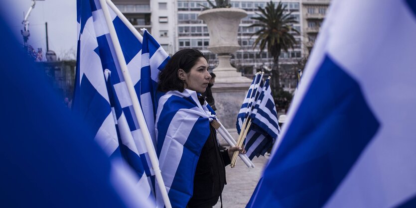 Eine Frau hält auf einer Demonstration sehr viele griechische Flaggen