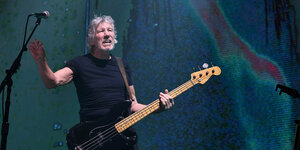 Roger Waters hängt ein Bass über der Schulter, er greift nach einem Mikrofon