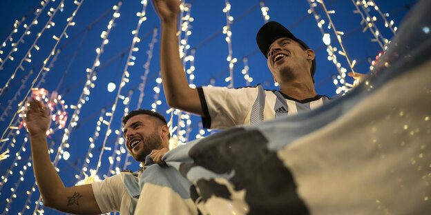 Zwei Männer halten die argentinische Flagge und lachen