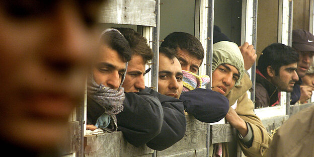 Männer mit Kapuzen gucken durch Fenster eines Bretterverschlags