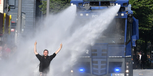 Ein Demonstrant mit schwarzem Kapuzenpulli steht vor einem blauen Wasserwerfer der Polizei, der im Einsatz ist