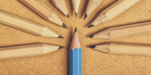 Viele Bleistifte mit braunem Lack gruppieren sich um einen Bleistift mit blauem Lack auf einer braunen Tischfläche