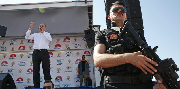 Wahlkampf Türkei Suruc - links ein Mann auf einer Bühne, es ist der türkische Präsident Erdogan, rechts vorne ein Mann mit Waffe