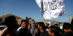 Mehrere Männer auf der Straße, einer hält eine weiße Fahne mit schwarzer Schrift gegen den blauen Himmel