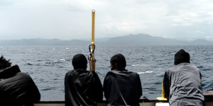 Flüchtlinge auf einem Boot schauen aufs Festland