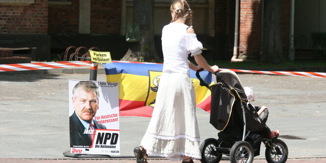 Eine junge Frau in einem altmodischen Kleid vor einem NPD-Wahlplakat